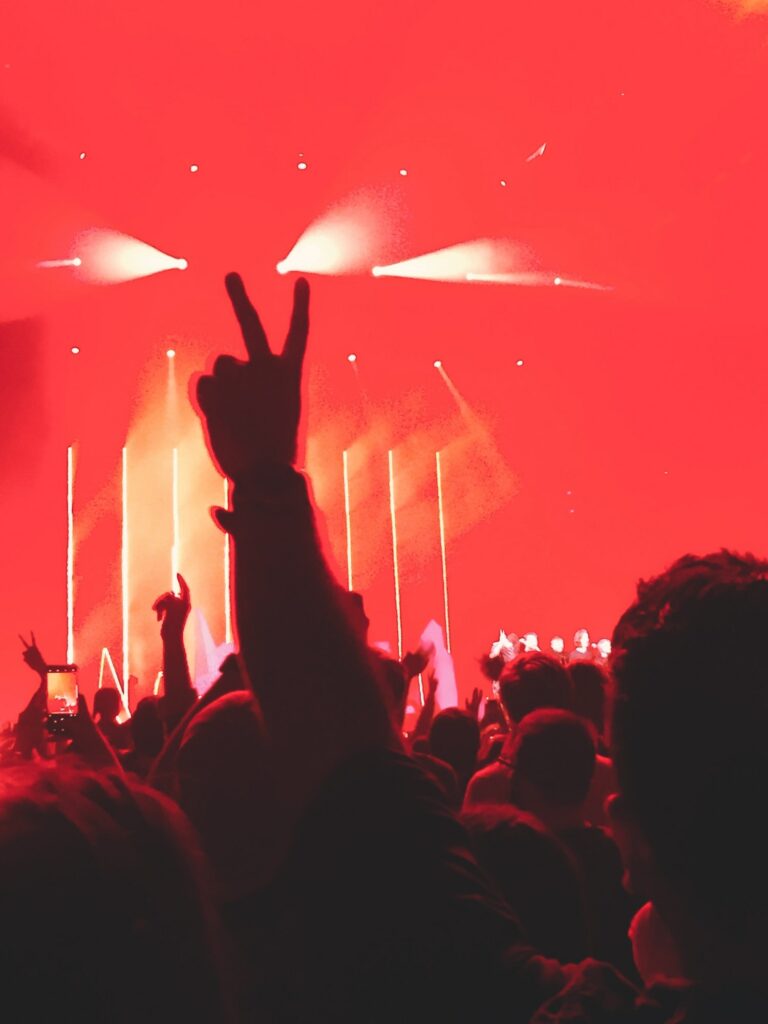 A man throwing up a peace sign at a music concert with a red glow from the lights